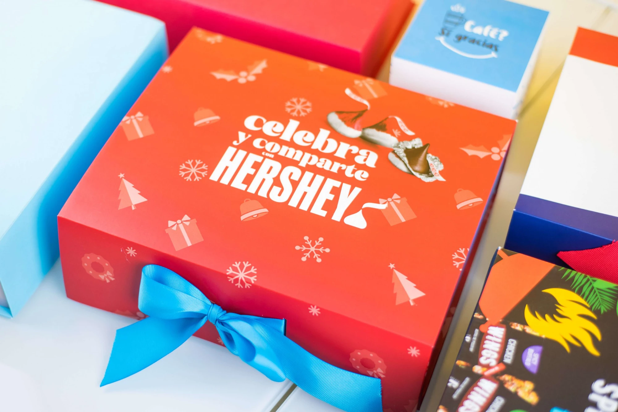 Caja roja navideña de Hershey con el mensaje Celebra y comparte y lazo azul