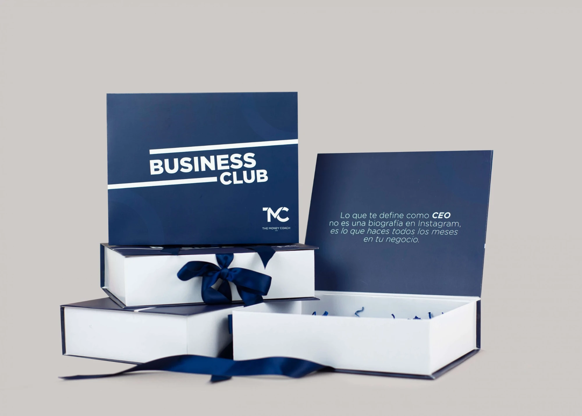 Cajas Business Club de The Money Coach en azul marino con lazo y mensaje impreso en el interior de la tapa